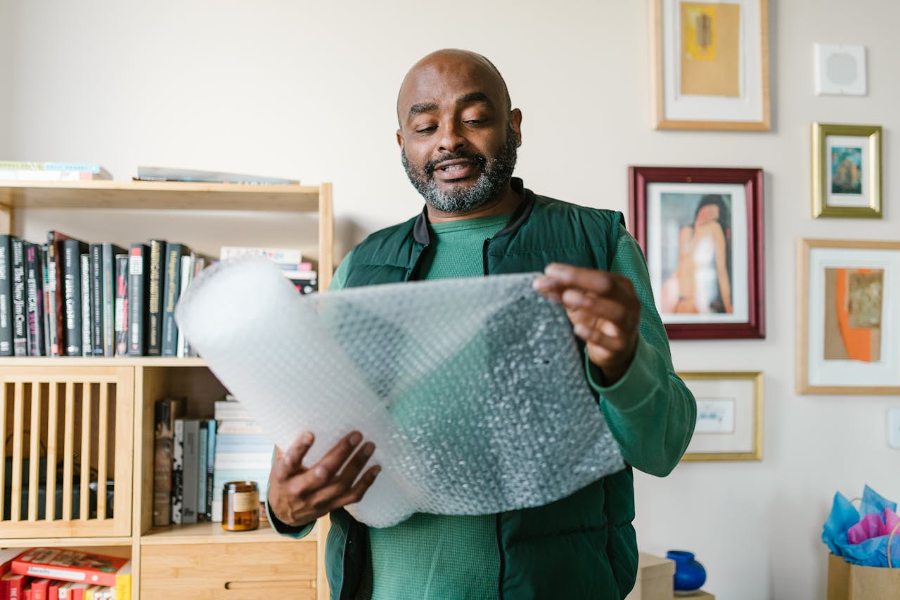 African American man holding and inspecting bubble wrap at home.